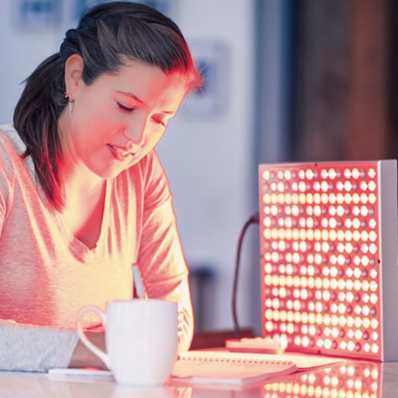 Woman writing on a note pad while doing Red Light Therapy with the TrueLight® Energy Square