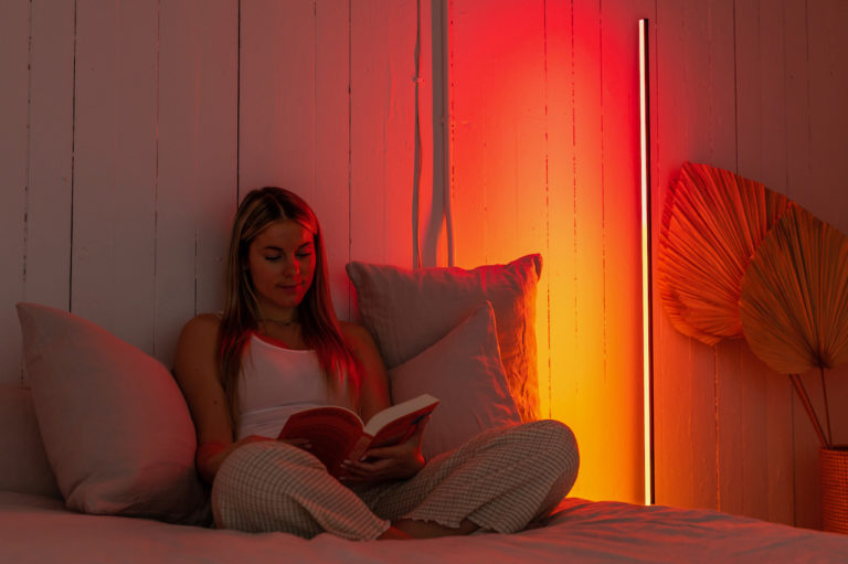 Image of woman on a bed reading a book next to Luna Red® Luminaire