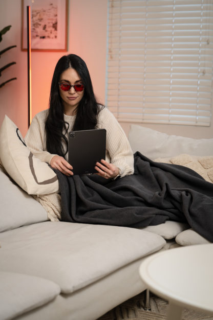 Image of woman on couch reading with Luna Red® Blanket and Luna Red® Luminaire